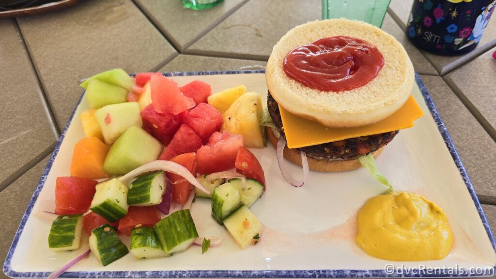 Veggie Burger and fresh fruit and veggies sitting on a white plate.