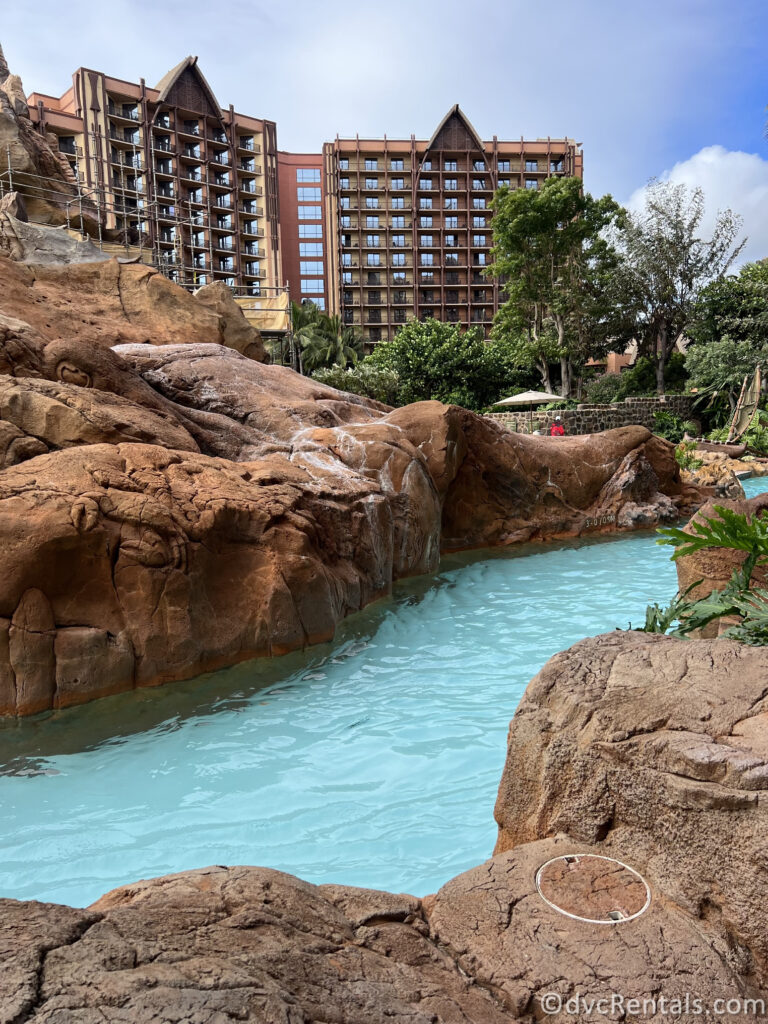 Lazy River between brown rocks at Aulani with the building in the background.