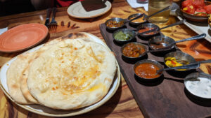 Sanaa Bread Service. Pieces of Naan sit on a plate next to a wooden board holding 11 different dips in little silver cups.