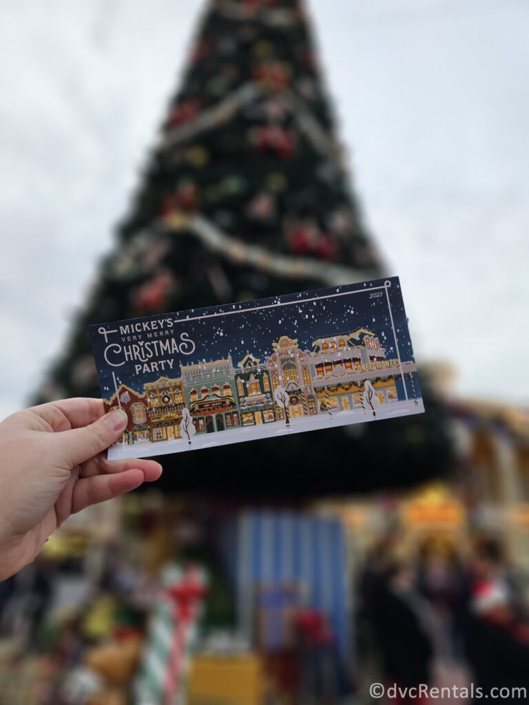 Map of Mickey's Very Merry Christmas Party being held up in front of a large Christmas Tree.