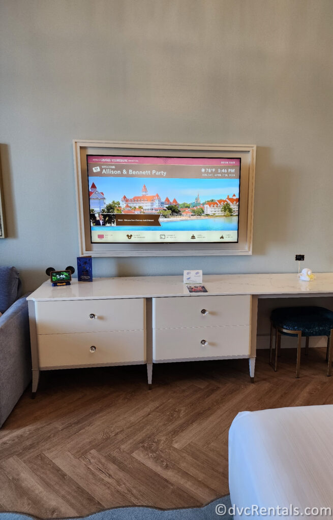 White desk in the Resort Studio with a TV hanging above on the wall. The tv welcomes the traveling party to the room.