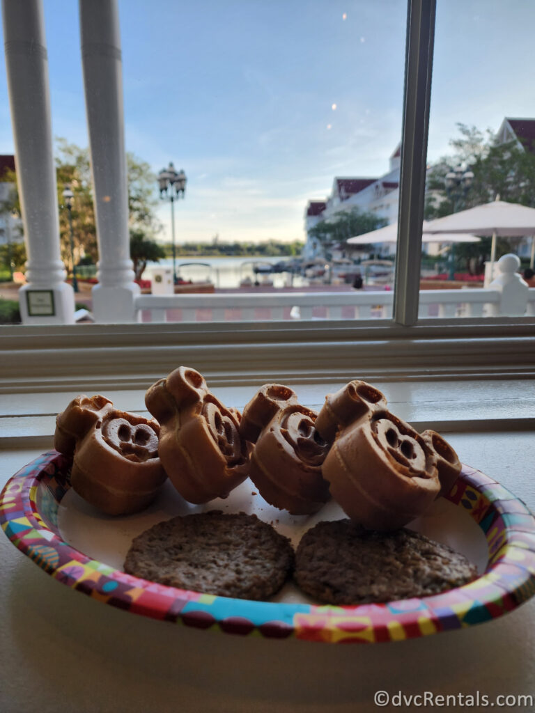 Mickey Waffles and Sausage Patties sitting on a paper plate in front of a window looking out at the boat dock at Disney's Grand Floridian.