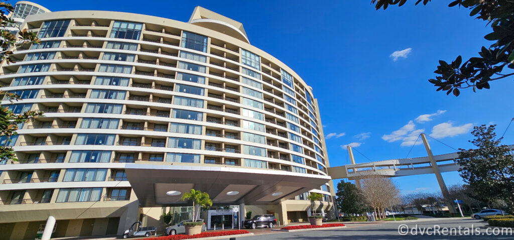 Exterior of Bay Lake Tower at Disney's Contemporary Resort. The large beige building is covered in hotel room windows, and has a suspended walking path to the right of the path.