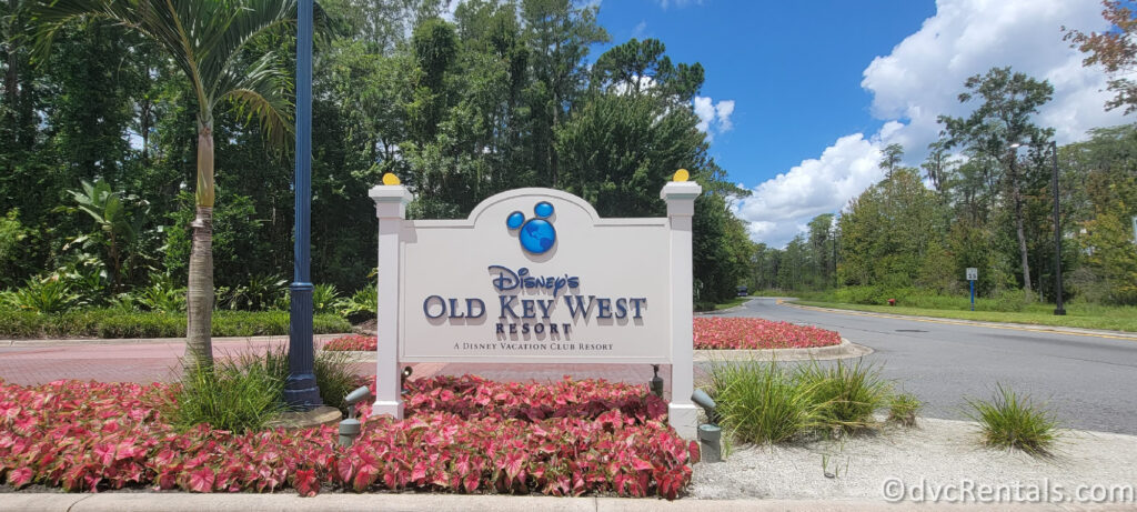 A sign at the entrance of Disney's Old Key West Resort. The sign is white with a blue logo of Mickey Mouse's head, and it reads "Disney's Old Key West Resort, A Disney Vacation Club Resort."