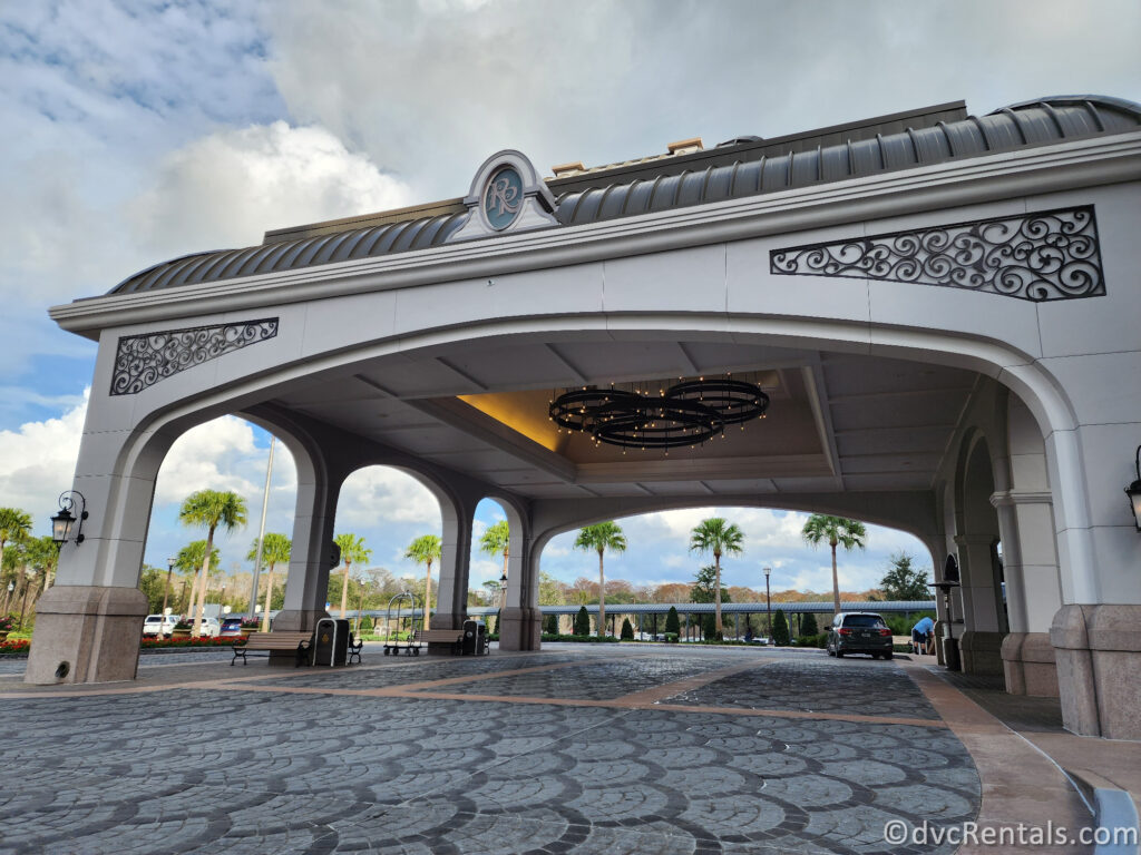 A grand entrance to Disney's Riviera Resort, featuring a curved archway with a decorative light fixture and stone pavers leading up to the entrance.