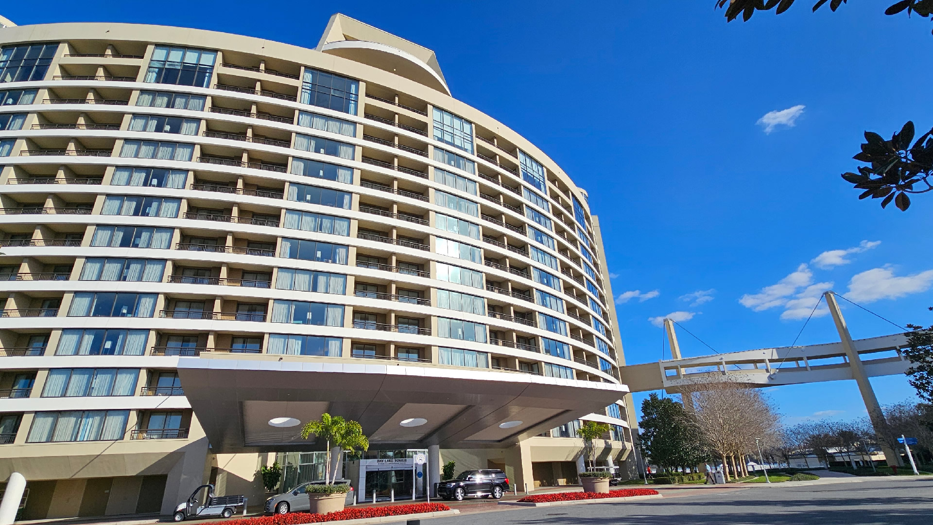 Exterior of Bay Lake Tower at Disney's Contemporary Resort. The large beige building is covered in hotel room windows, and has a suspended walking path to the right of the path.