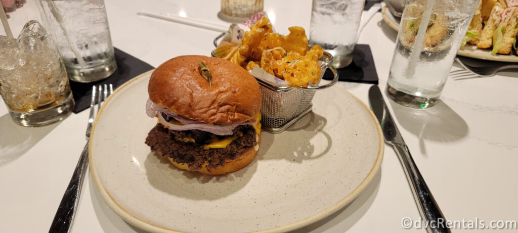 Steakhouse 71 burger sitting on a white plate. There are waffle fries covered in parmesan cheese sitting in a small metal basket beside the burger.