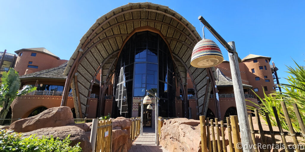 Entrance to Disney's Animal Kingdom villas - Kidani Village. The entrance features a large, thatched roof supported by wooden beams, and a large glass window behind it.