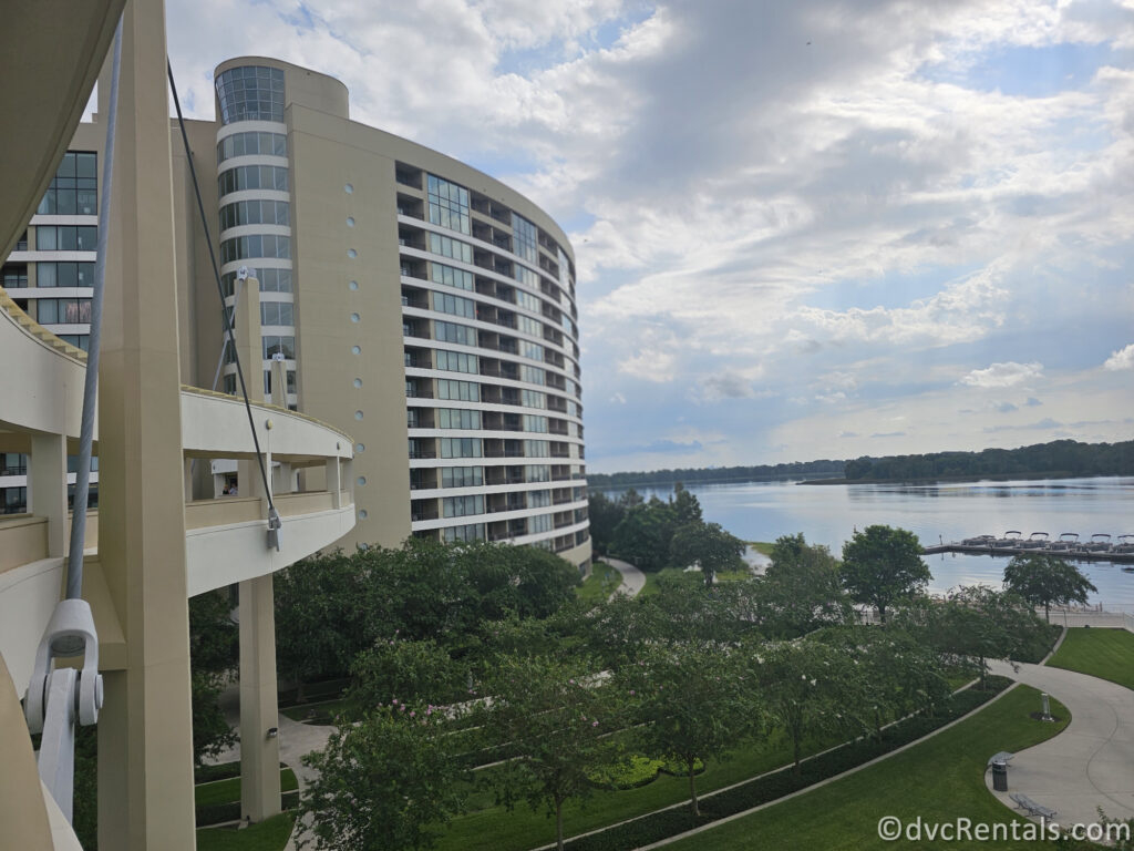 A view of Bay Lake Tower at Disney's Contemporary Resort from the Disney Skyliner. The hotel tower is a curved, beige-colored building with balconies overlooking a lush green landscape.