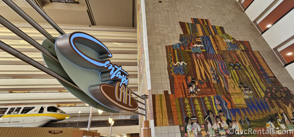 Sign for Contemp Cafe. The lettering is done in blue metal script. There is a colorful mural to the right of the restaurant sign, and a yellow and right monorail car to the left of the sign.