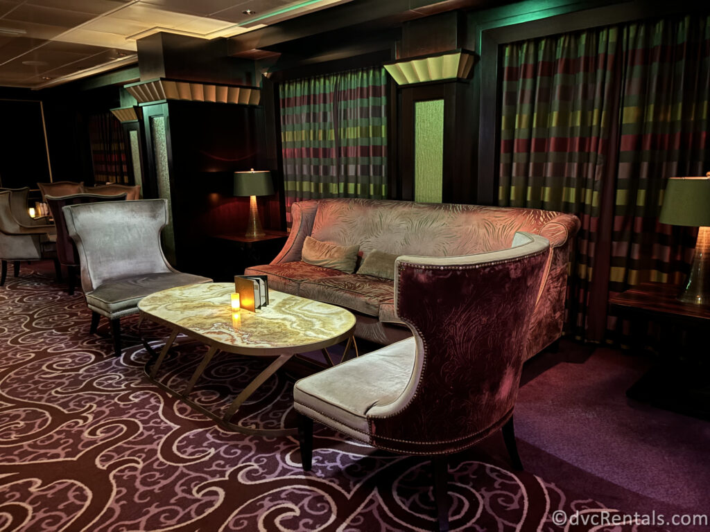 Inside the Ensemble Lounge onboard the Celebrity Reflection. Dark purple and gold carpets cover the floor, with large silver couches and chairs sitting around a gold coffee table.