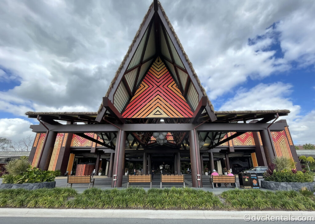 Main entrance to Disney's Polynesian Village Resort. The entrance features a large, triangular roof with intricate patterns in shades of red, orange, and yellow.