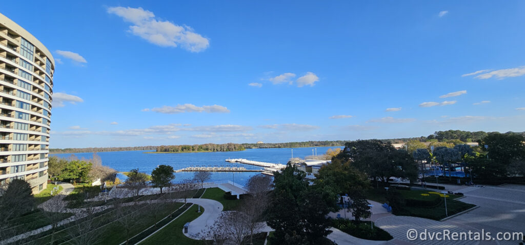 A panoramic view of Bay Lake Tower at Disney's Contemporary Resort. The hotel tower is a curved building with balconies overlooking a large lake and dock.