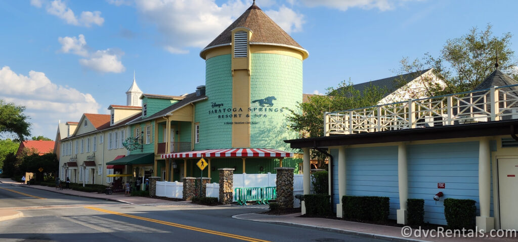 Disney's Saratoga Springs Resort & Spa. The resort features a charming, Victorian-style building with a green tower and a red and white striped awning over the entrance.