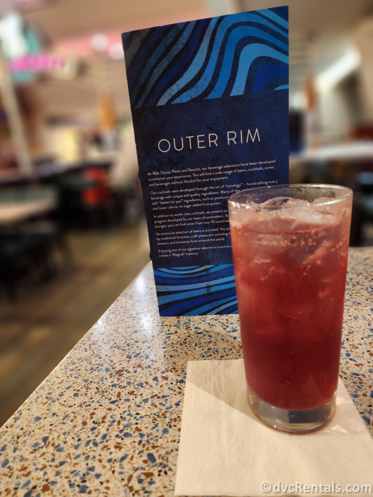 Navy Blue Cocktail menu for Outer Rim sitting on a table with a purple mocktail.