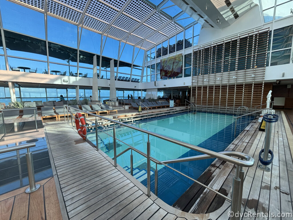 Pool Deck in the Solarium onboard the Celebrity Reflection. The bright blue water of the pool is surrounded by a wooden pool deck.