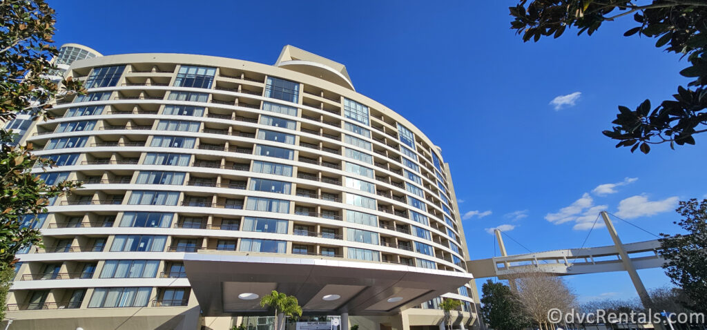 Entrance to Bay Lake Tower. The building is surrounded by lush greenery and features a pedestrian bridge connecting it to Disney's Contemporary Resort in the background.