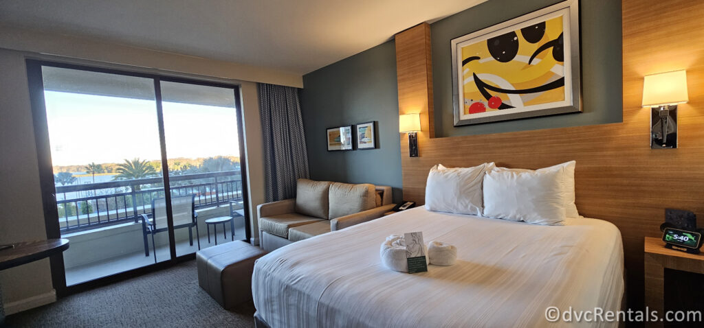 Current interior of the Studio at Bay Lake Tower. A queen sized bed sits next to a brown couch. There is a modern print of Mickey Mouse above the bed.