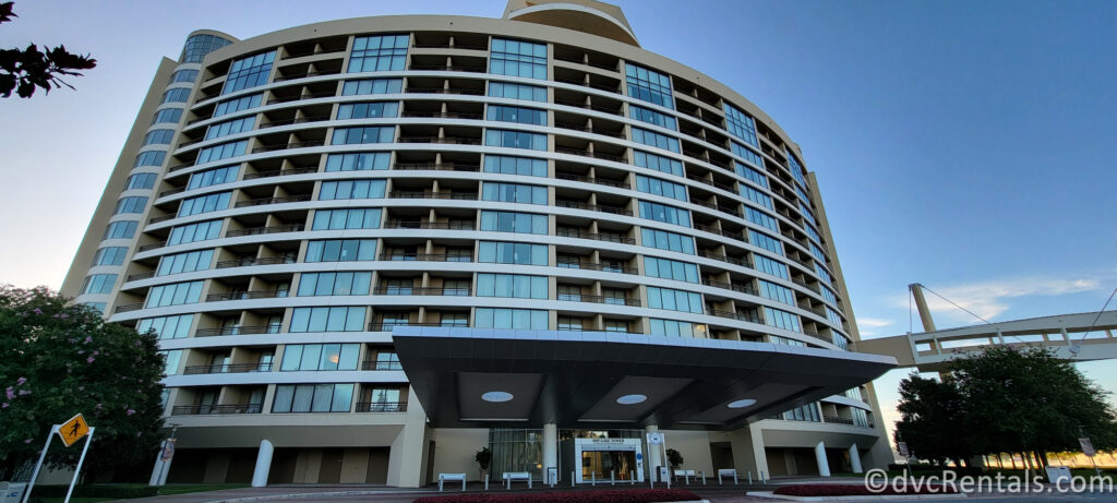 Exterior of Bay Lake Tower at Disney's Contemporary Resort. The large beige building is covered in hotel room windows, and has a suspended walking path to the right of the path.