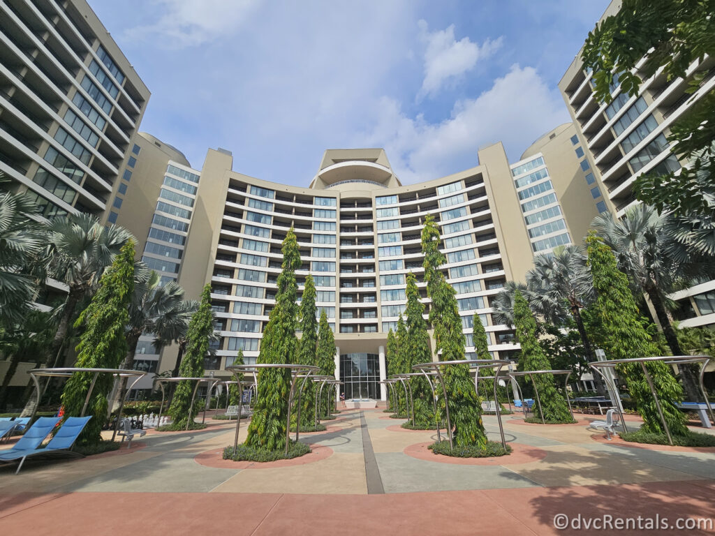 Back of Bay Lake Tower at Disney's Contemporary Resort. The large beige building is covered in hotel room windows, and there are lines of trees in front of the building.