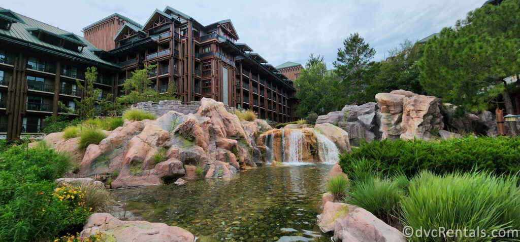 Disney's Wilderness Lodge. The resort's building is visible in the background, with a large waterfall flowing into a pond in the foreground.