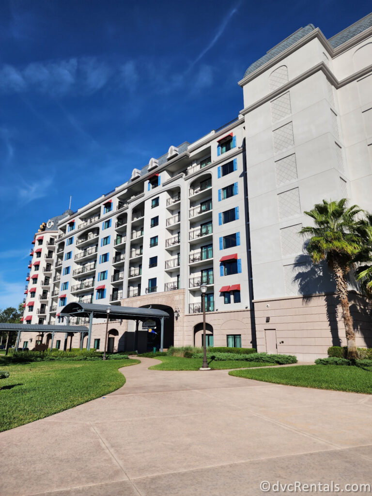 Exterior of Disney's Riviera Resort. The resort's building is a large, white structure with blue shutters and balconies.