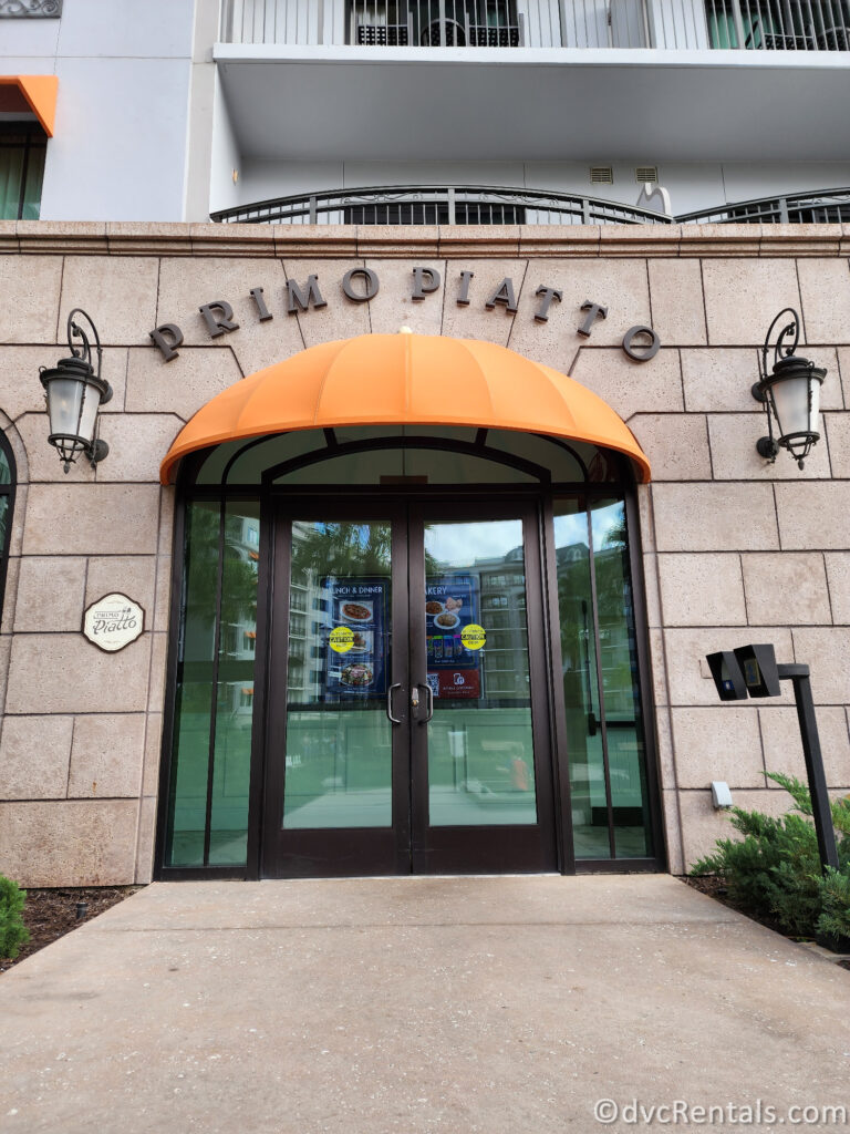 The entrance to Primo Piatto. The restaurant has a brick facade, a large orange awning, and double glass doors.