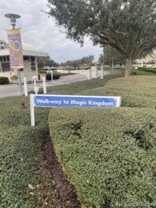 Blue sign with white lettering that reads "Walkway to Magic Kingdom" sitting in the bushes at Bay Lake Tower.