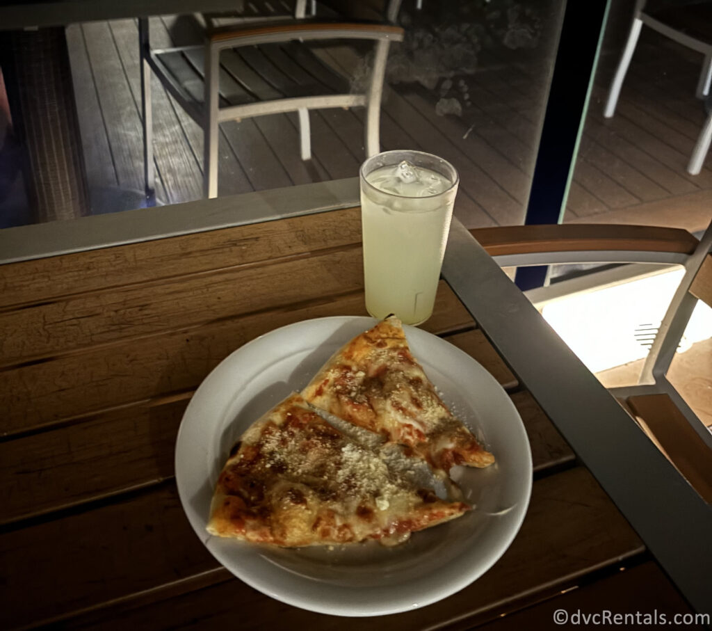 Two slices of pepperoni pizza and lemonade in a clear glass sitting on a wooden table.