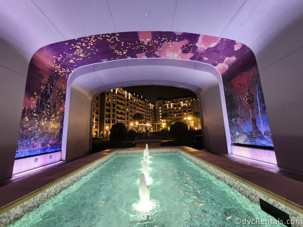 A nighttime view of the Skyliner station entrance at Disney's Riviera Resort. The archway above the entrance is illuminated with a colorful mosaic featuring Tangled lanterns.