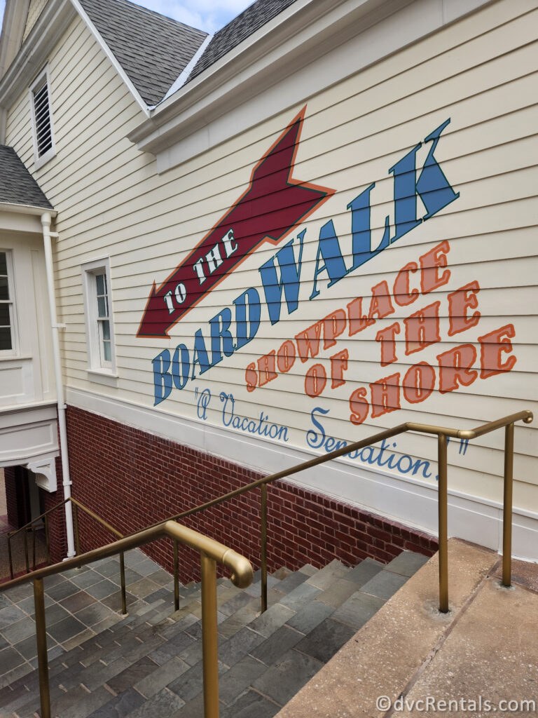 A colorful mural on the side of a building, advertising "Disney's Boardwalk." The mural features a red arrow pointing towards the boardwalk, and the text "TO THE BOARDWALK SHOWPLACE OF THE SHORE" in bold, stylized letters.