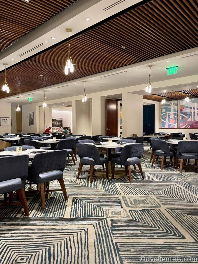 Interior of Steakhouse 71. The 70's 70-themed restaurant is filled with short blue fabric chairs around white tables, sitting on a black and white geometric carpet.