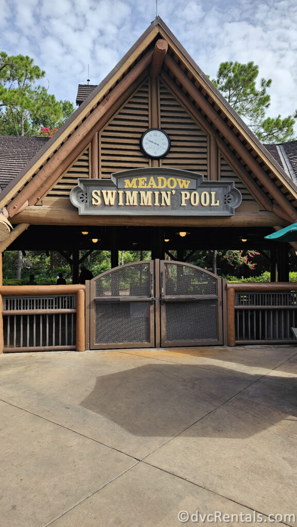 A wooden entrance to the Meadow Swimmin' Pool at Disney's Fort Wilderness Resort. The entrance has a rustic design with a gabled roof and a clock.