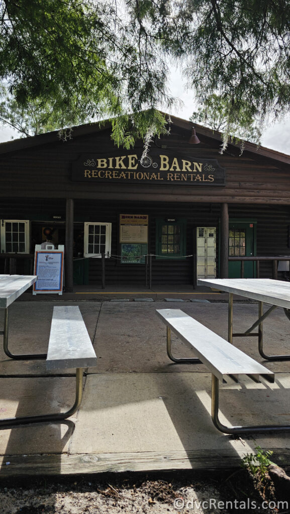 A wooden building labeled "BIKE BARN RECREATIONAL RENTALS" with a shaded patio area featuring picnic tables.