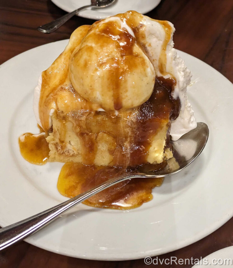 ‘Ohana break pudding dessert served on a white plate with a silver spoon, ice cream and golden-brown caramel sauce.