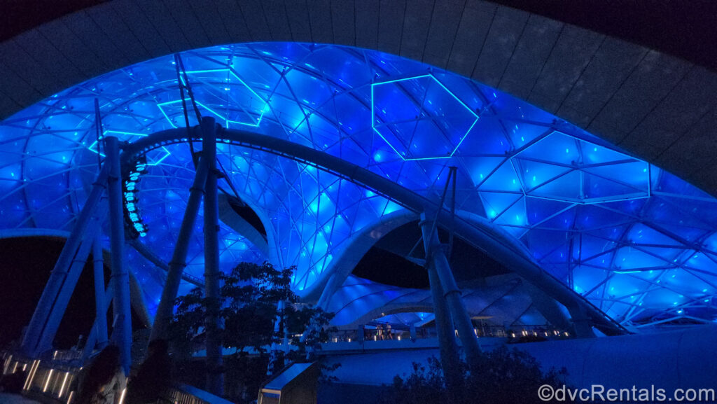 Tron at Magic Kingdom at night. The ride canopy is lit up blue, and ride vehicles lit up neon blue race along the coaster tracks.