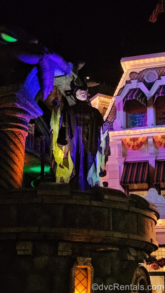 Maleficent in her black, purple, and green costume performs on a parade float designed to look like a stone castle turret during Mickey’s Boo-To-You Halloween Parade.