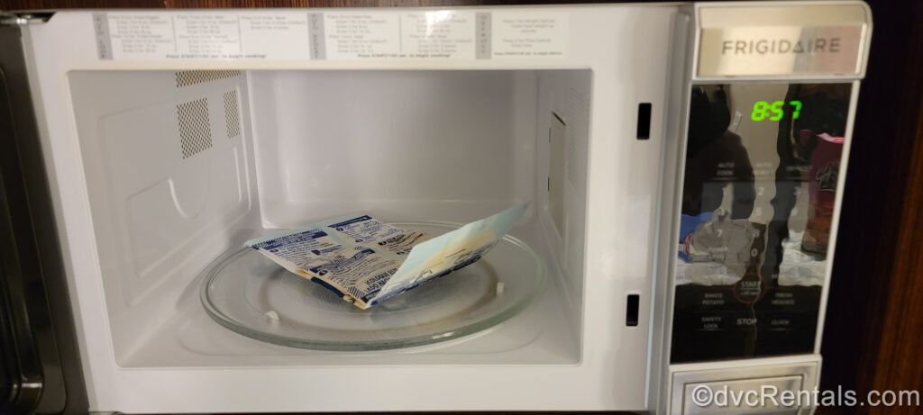 An un-popped bag of microwave popcorn placed on the inside glass tray of the microwave in a Studio kitchenette at Bay Lake Tower at Disney’s Contemporary Resort. The door of the microwave is open, so the white interior is visible.