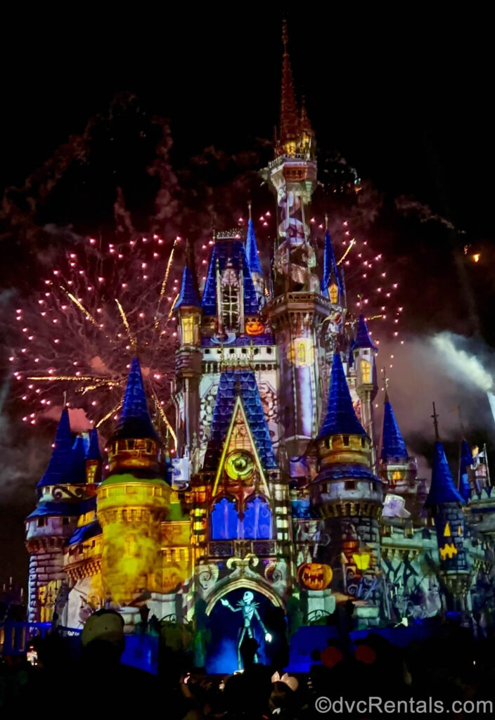 Jack Skellington is seen in front of Cinderella Castle. The castle is illuminated by pink and gold fireworks as well as Halloween-themed projection special effects featuring orange jack-o’-lanterns.