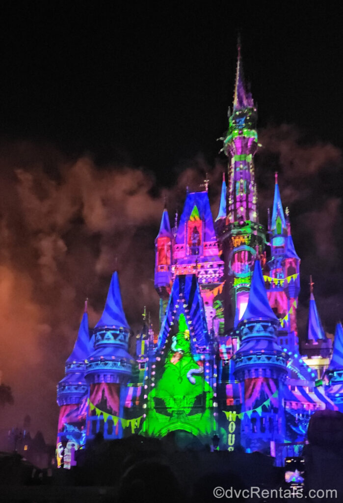 Colorful Halloween-themed projections featuring neon green Oogie Boogie from The Nightmare Before Christmas light up Cinderella Castle at Magic Kingdom.