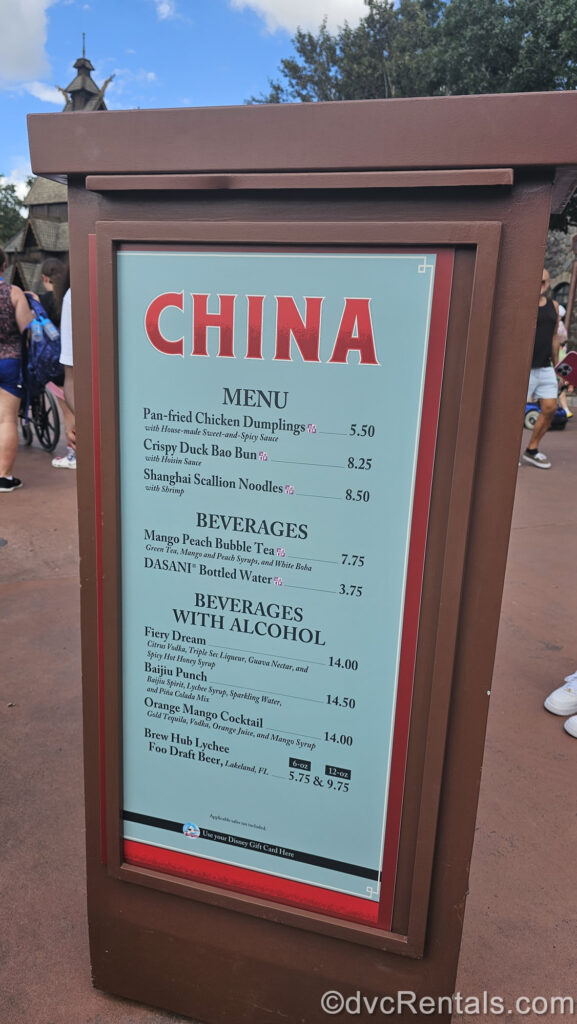 The brown, blue, and red menu board for the China booth. There are descriptions of the different food and drink options, as well as pricing displayed on the menu board.