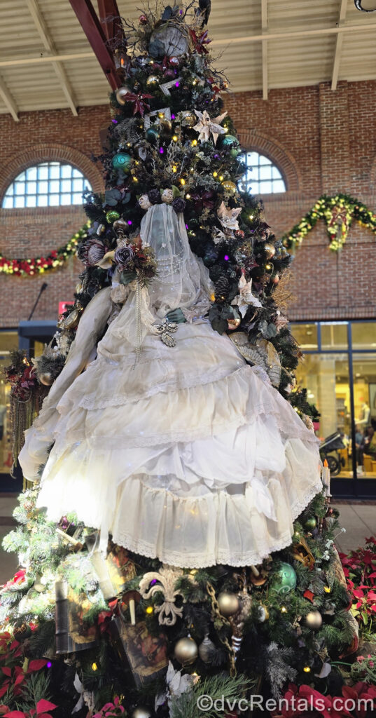 The Haunted Mansion themed Christmas Tree at Disney Springs. The tree is decorated with purple, green, and silvery ornate ornaments, with a large green bride in a white wedding gown holding a bouquet of dried purple and brown flowers.