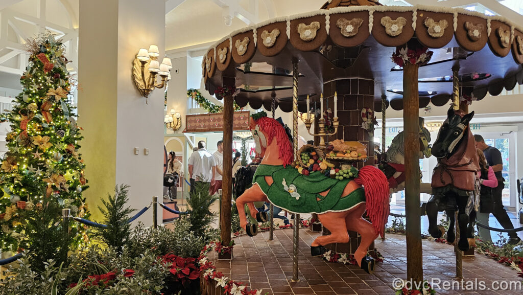 A gingerbread carousel inspired by Disney’s cartoon version of A Christmas Carol is on display at Disney’s Beach Club Villas. The multicolored horses on the carousel are designed to represent the characters of the film, and to the left is a large Christmas tree decorated with pastel nautical-themed ornaments.