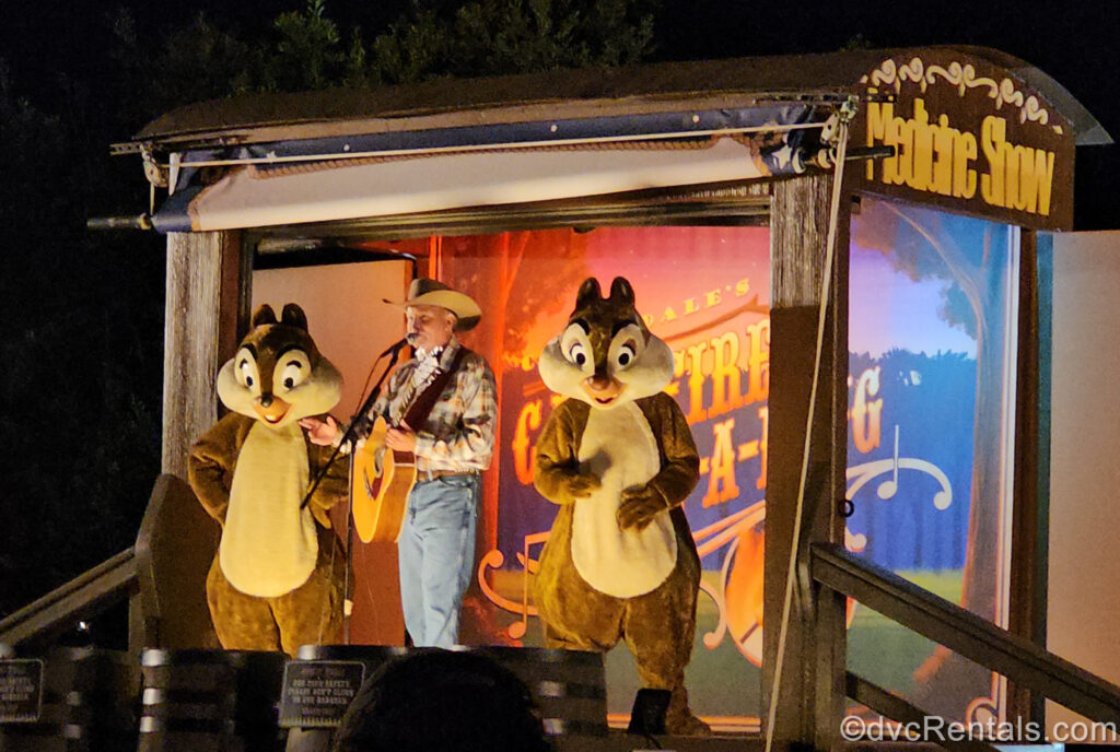 Characters Chip ‘N’ Dale and a cowboy singer with a guitar perform a sing along on an old wooden covered wagon turned into a stage.