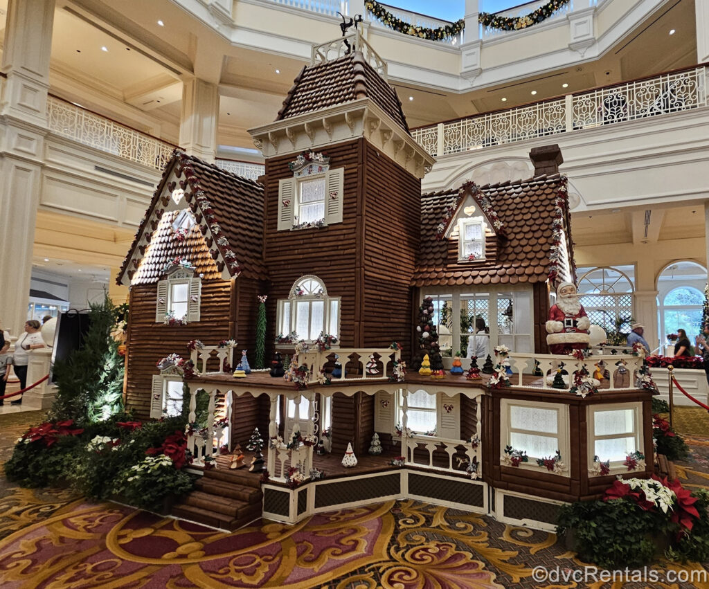 A life-size gingerbread house at Disney’s Grand Floridian Resort & Spa. The house is decorated with small Christmas trees inspired by various Disney characters, as well as a Santa statue and green and red foliage.