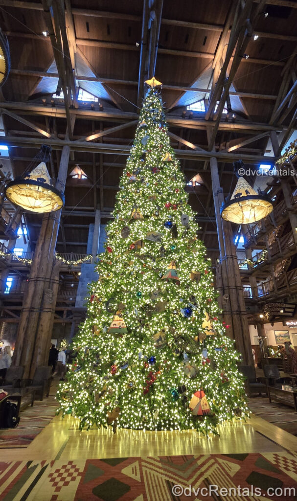 A very tall green Christmas tree decorated with red, green, brown, and blue ornaments and white lights is on display in the lobby of Disney’s Wilderness Lodge.