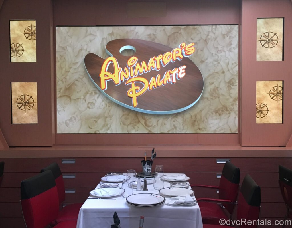 The words “Animator’s Palate” are displayed in brown and yellow font. Underneath there is a dining table with a white tablecloth and art-inspired plates and utensils. Red and black chairs inspired by Mickey Mouse are pulled up to the table.