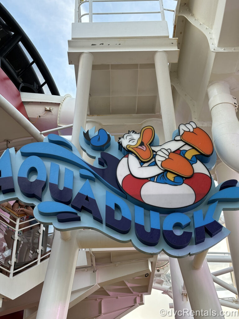 Donald Duck is depicted in a blue bathing suit and red and white striped inner tube on the blue sign for the AquaDuck water coaster.