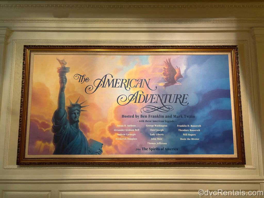 A sign for The American Adventure attraction at World Showcase in EPCOT displays the Statue of Liberty and a bald eagle in the sunset, as well as information about the historical figures included in the show hosted by Ben Franklin and Mark Twain.