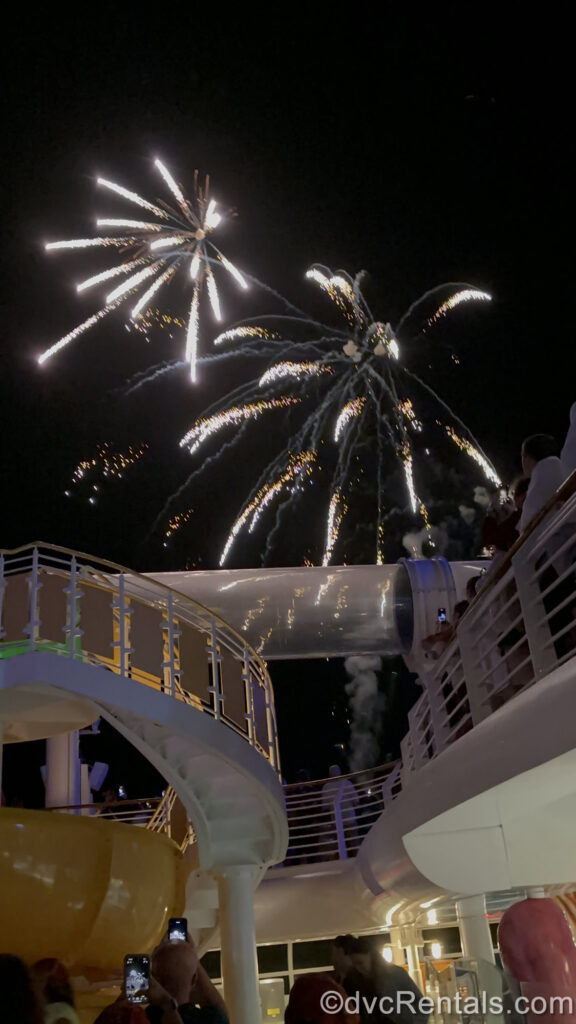 White and gold fireworks sparkle in the night sky over the deck of a Disney cruise ship.